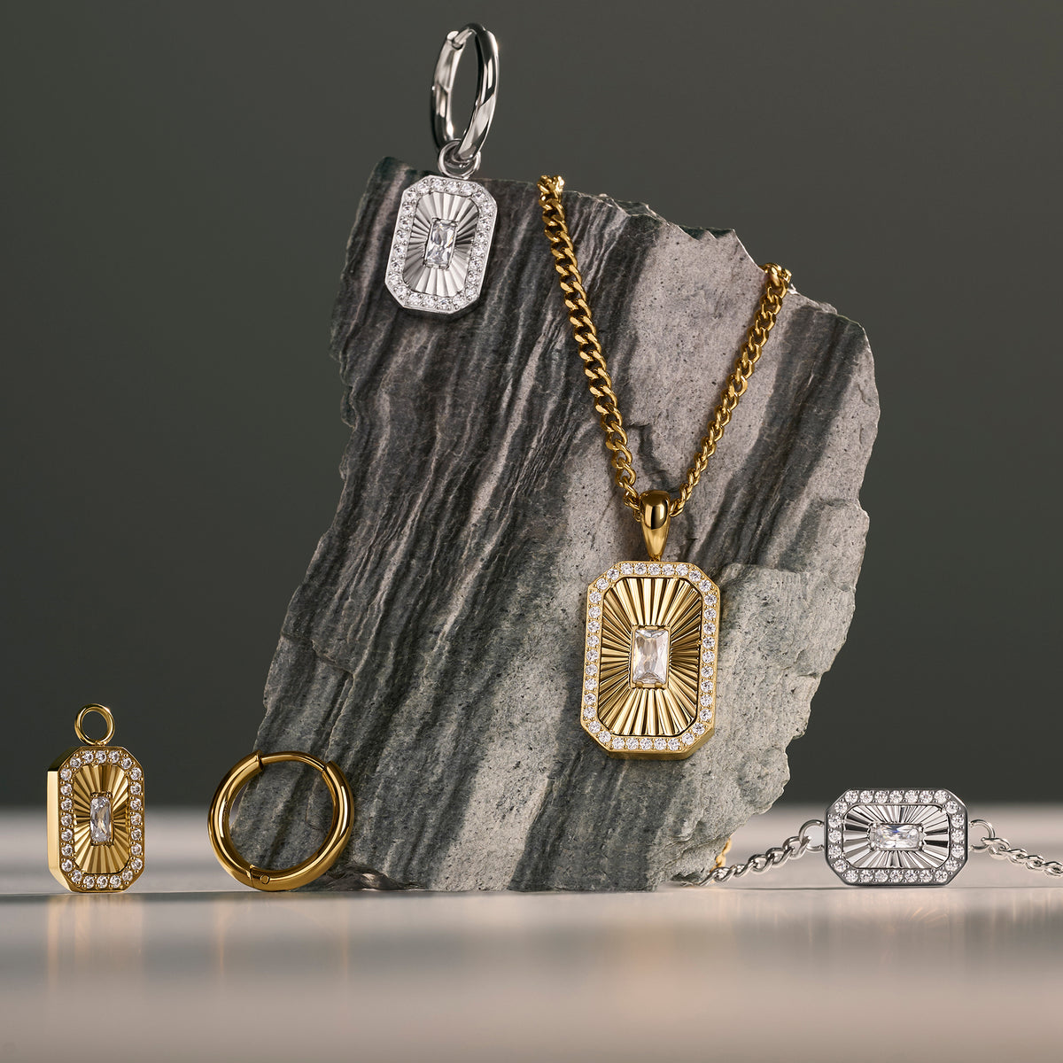 Gold and silver rectangular pendant jewelry with sunburst crystal detailing, displayed on a dark gray stone slab against a dark gray background. Jewelry by Mia Bijoux Canada.
Bijou à pendentif rectangulaire doré et argenté à motif rayonnant serti de cristaux, présenté sur une dalle de pierre gris foncé sur fond gris foncé. Bijoux par Mia Bijoux Canada.