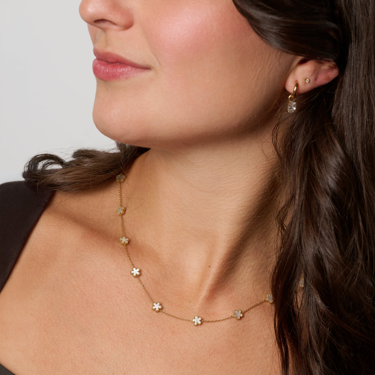 A close-up of a woman wearing a delicate gold necklace with small flower charms and gold earrings. Waterproof, stainless steel and allergy free. By MIAJWL.

Gros plan d'une femme portant un collier doré délicat orné de petites fleurs et des boucles d'oreilles dorées. Résistant à l'eau, en acier inoxydable et hypoallergénique. Par MIAJWL.
